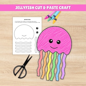 May include: A pink jellyfish craft with rainbow tentacles, a black pair of scissors, and a sheet of instructions. The text "JELLYFISH CUT & PASTE CRAFT" is at the top. Crayons in pink, blue, yellow, and green are also present.