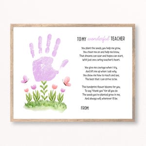 May include: A framed print with a light brown wooden frame. The print features a lavender handprint above a watercolor illustration of flowers and butterflies. Text reads "TO MY wonderful TEACHER" and a poem.