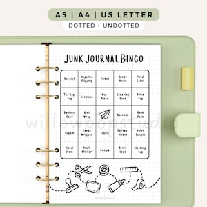 May include: A printable Junk Journal Bingo game sheet inside a light green binder. The page features a five-by-five grid with text prompts, a paper airplane icon, and bottom illustrations of craft supplies including scissors, tape, and a ruler.