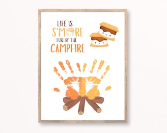 May include: A framed print with the text "LIFE IS S'MORE FUN BY THE CAMPFIRE". The image features a campfire made of handprints and logs, with two cartoon s'mores above. The print has a wooden frame.