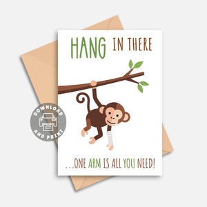 May include: A greeting card with a brown monkey hanging from a branch. The text "HANG IN THERE" is above the monkey, and "...ONE ARM IS ALL YOU NEED!" is below. The card is on a light brown envelope.