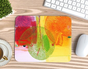 Può includere: Tappetino per mouse di arte astratta con un design colorato. Il tappetino presenta un vivace mix di tonalità rosse, rosa, arancioni, verdi e gialle. Un mouse e una tastiera bianchi sono visibili sullo sfondo.
