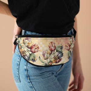May include: A floral fanny pack featuring a watercolor design of tulips in shades of pink, purple, and yellow. The bag has a black zipper and trim, and a checkered background. The bag is worn around the waist.
