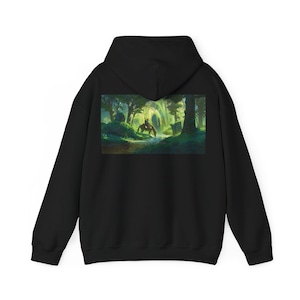 May include: Black hooded sweatshirt featuring a vibrant forest scene with a person on horseback. The artwork depicts a lush green forest with sunlight streaming through the trees. A serene landscape design for nature lovers.