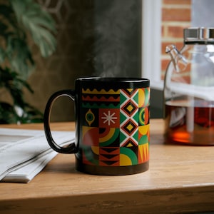 May include: Black ceramic mug with a geometric pattern in red, yellow, green, and blue. The mug is filled with a hot drink and steam is rising from the top.