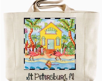 May include: A beige canvas tote bag with a colorful illustration of a yellow house with a white picket fence, palm trees, and pink flamingos. The text "St. Petersburg, FL" is printed on the bag.