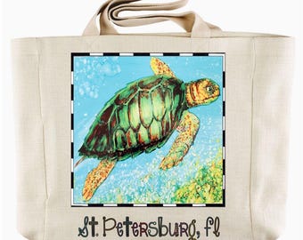 May include: A beige tote bag featuring a colorful illustration of a sea turtle swimming in the ocean. The turtle has a green and brown shell with yellow accents. The text "St. Petersburg, fl" is printed at the bottom.