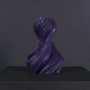 K&ouml;nnte beinhalten: Eine dunkelviolette Vase mit einem wirbelnden, strukturierten Design und funkelnden Details. Die Vase steht auf einer schwarzen Oberfl&auml;che. Die dekorative Vase ist ein modernes Wohnaccessoire. Die H&ouml;he der Vase betr&auml;gt ca. 20 cm.