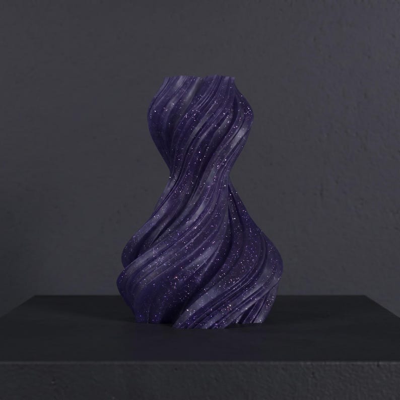 K&ouml;nnte beinhalten: Eine dunkelviolette Vase mit einem wirbelnden, strukturierten Design und funkelnden Details. Die Vase steht auf einer schwarzen Oberfl&auml;che. Die dekorative Vase ist ein modernes Wohnaccessoire. Die H&ouml;he der Vase betr&auml;gt ca. 20 cm.
