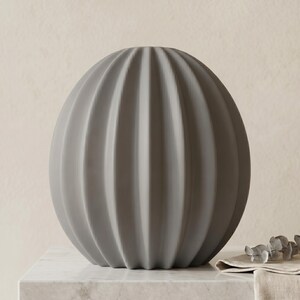 May include: A grey, spherical decorative vase with vertical ribbed detailing. The vase is made of a matte material and sits on a marble surface. The vase has a modern, minimalist design.