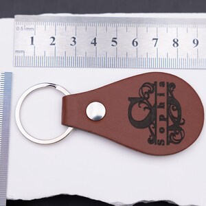 Personalisierter Schlüsselanhänger aus braunem Kunstleder mit Gravur und Maßangaben zur Orientierung. Die Lineale zeigen eine Länge von etwa 9 cm und eine Breite von rund 4,5 cm – kompakt, aber dennoch gut sichtbar. Der Anhänger vereint elegantes Design, individuelle Gravur und Funktionalität und eignet sich perfekt für Autoschlüssel, Haustürschlüssel oder als personalisiertes Geschenk.
