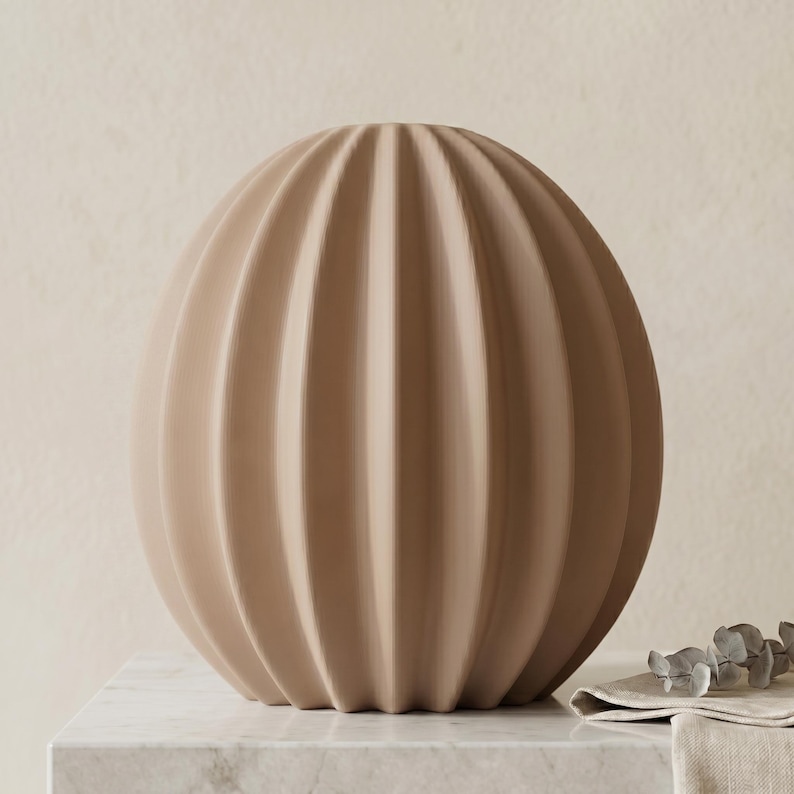 May include: A beige, spherical decorative vase with vertical, ribbed detailing. The vase has a rounded shape and a neutral colour, suitable for various interior design styles. It is placed on a marble surface.