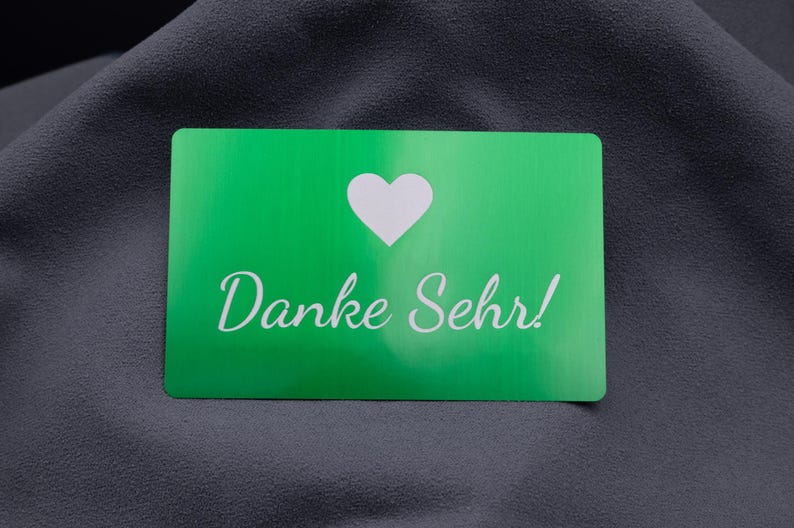 Grüne Metall-Visitenkarte mit lasergraviertem Herzsymbol und Schriftzug „Danke Sehr!“. Die Karte wirkt modern und stilvoll, ideal als hochwertige Beigabe zu Bestellungen, als Kundendankeschön oder zur Markenbindung. Die Aluminiumoberfläche ist langlebig, stabil und vermittelt Exklusivität, wodurch sich diese Karte von herkömmlichen Papierkarten deutlich abhebt.
