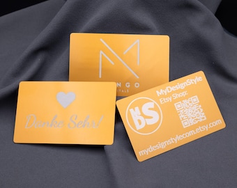 Wizytówka metalowa, aluminiowa, złota, ciemna, personalizowana grawerunkiem laserowym zawierającym imię, logo, grafikę i kod QR.
