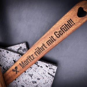 Holzkochlöffel mit Gravur „Moritz rührt mit Gefühl!!!“ und Löffelsymbol, kombiniert mit zweitem Löffel „Sophia wendet mit Liebe!“. Beide Küchenutensilien bestehen aus robustem Akazienholz mit schöner Maserung. Durch Gravur personalisierbar mit Namen oder Spruch – stilvoll, langlebig und individuell.