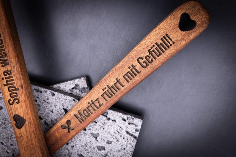 Holzkochlöffel mit Gravur „Moritz rührt mit Gefühl!!!“ und Löffelsymbol, kombiniert mit zweitem Löffel „Sophia wendet mit Liebe!“. Beide Küchenutensilien bestehen aus robustem Akazienholz mit schöner Maserung. Durch Gravur personalisierbar mit Namen oder Spruch – stilvoll, langlebig und individuell.