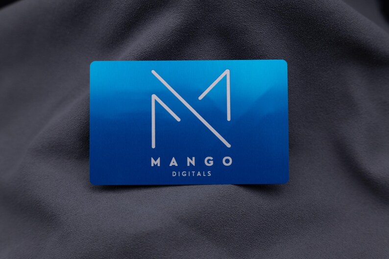 Exklusive Mango-Digitals-Visitenkarte aus Aluminium in Blau mit modernem Logo-Design. Die klare Gravur und die elegante, matte Metalloberfläche vermitteln Professionalität und Qualität. Mit Standard-Visitenkartengröße und stabiler Verarbeitung eignet sich die Karte ideal für Firmen, die ihre Marke mit einem langlebigen und auffälligen Auftritt repräsentieren möchten.