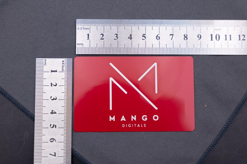Rote Metallkarte mit Mango-Digitals-Logo, dargestellt mit Lineal zur Größenangabe. Das Format entspricht einer klassischen Kreditkarte (8,6 × 5,4 cm). Langlebig, stabil und edel – ideal als exklusive Businesskarte oder kreative Werbekarte.