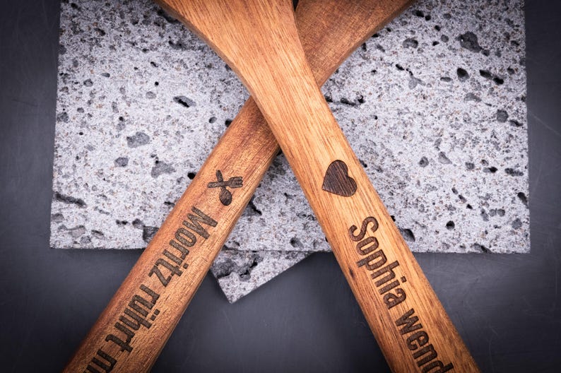 Eng gefasste Aufnahme des 2er-Kochlöffelsets mit Gravuren „Sophia wendet mit Liebe!“ und „Moritz rührt mit Gefühl!!!“. Die dunkle Gravur wirkt präzise und kontrastreich auf dem hellbraunen Akazienholz. Perfekt als personalisiertes Geschenkset für Küche, Grill oder Backfreunde.