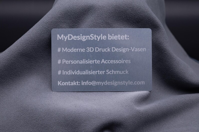 Hochwertige Aluminium-Visitenkarte in Silber mit eingravierten Informationen zu angebotenen Produkten: moderne 3D-Druck-Vasen, personalisierte Accessoires und individueller Schmuck. Darunter die E-Mail-Adresse des Shops. Die gravierte Metallkarte ist robust und elegant, perfekt für Unternehmer und Designer, die sich mit exklusivem Material und modernem Look von klassischen Papierkarten abheben möchten.