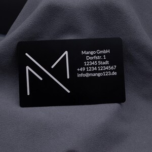 Schwarze Aluminium-Visitenkarte mit graviertem Firmenlogo und vollständigen Kontaktdaten. Eine exklusive Alternative zu klassischen Papierkarten, robust, modern und langlebig – perfekt für Business, Networking und professionelle Präsentation.