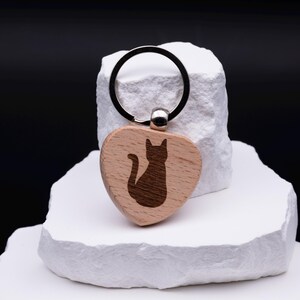 Schlüsselanhänger in Herzform aus Holz mit eingraviertem Katzenmotiv. Ein liebevoll gestaltetes Accessoire, ideal als Geschenkidee für Katzenliebhaber, Familie oder Freunde. Der Anhänger kann zusätzlich mit einem Namen oder Symbol graviert werden und wird so zu einem einzigartigen Unikat. Robustes Holz kombiniert mit feiner Gravur sorgt für ein nachhaltiges und stilvolles Alltagsaccessoire.