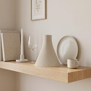 Peut inclure: Un vase beige textur&eacute;, &agrave; base large et sommet &eacute;troit, est pos&eacute; sur une &eacute;tag&egrave;re en bois, &agrave; c&ocirc;t&eacute; d'une assiette blanche, d'une petite tasse, d'un verre &agrave; vin et d'une longue bougie blanche. Une impression botanique encadr&eacute;e est accroch&eacute;e au mur.