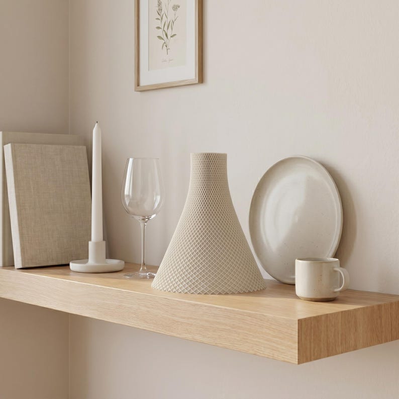 Peut inclure: Un vase beige textur&eacute;, &agrave; base large et sommet &eacute;troit, est pos&eacute; sur une &eacute;tag&egrave;re en bois, &agrave; c&ocirc;t&eacute; d'une assiette blanche, d'une petite tasse, d'un verre &agrave; vin et d'une longue bougie blanche. Une impression botanique encadr&eacute;e est accroch&eacute;e au mur.