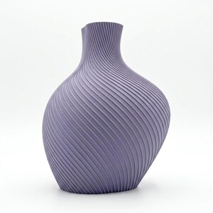 Puede incluir: Un jarr&oacute;n de color lavanda con un dise&ntilde;o texturizado &uacute;nico. El jarr&oacute;n tiene un cuerpo ancho y redondeado que se estrecha hacia un cuello estrecho. La superficie est&aacute; cubierta por una serie de l&iacute;neas diagonales y onduladas, creando un efecto acanalado. Un art&iacute;culo decorativo.