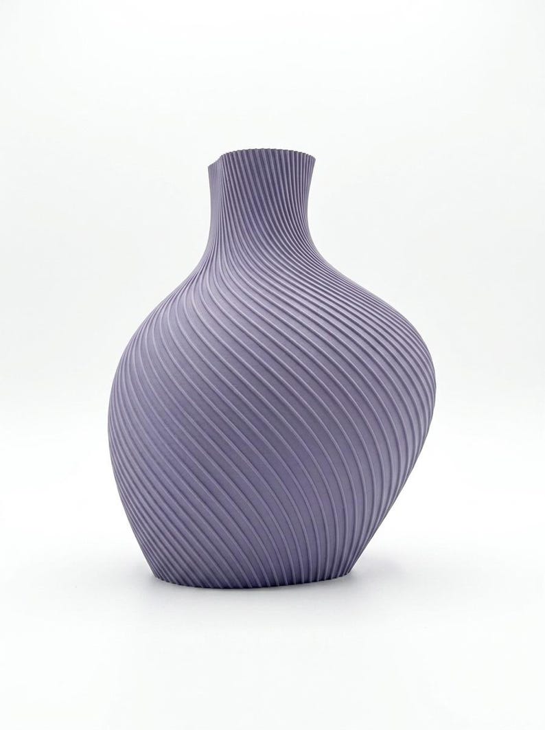 Puede incluir: Un jarr&oacute;n de color lavanda con un dise&ntilde;o texturizado &uacute;nico. El jarr&oacute;n tiene un cuerpo ancho y redondeado que se estrecha hacia un cuello estrecho. La superficie est&aacute; cubierta por una serie de l&iacute;neas diagonales y onduladas, creando un efecto acanalado. Un art&iacute;culo decorativo.
