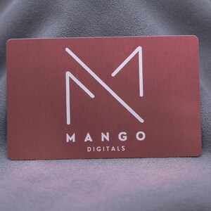 Businesskarte aus roségoldenem Aluminium mit graviertem Mango-Digitals-Logo. Die Metallkarte überzeugt durch minimalistisches Design, edle Oberfläche und langlebige Qualität. Ideal für Start-ups, Designer und Unternehmen, die eine auffällige und moderne Alternative zur klassischen Papierkarte suchen.