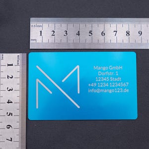 Visitenkarte aus Aluminium in Blau mit Mango-Logo und Kontaktdaten, daneben zwei Lineale zur Größenangabe (ca. 8,6 × 5,4 cm). Die stabile Metallausführung mit abgerundeten Kanten hebt sich deutlich von herkömmlichen Papierkarten ab. Ideal für Geschäftskunden und Firmen, die Wert auf Exklusivität, Langlebigkeit und ein modernes, professionelles Design legen.
