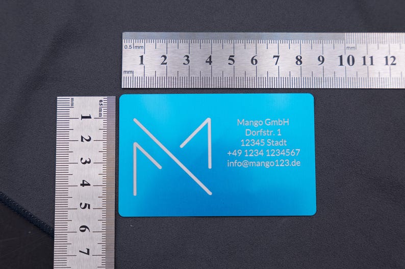 Visitenkarte aus Aluminium in Blau mit Mango-Logo und Kontaktdaten, daneben zwei Lineale zur Größenangabe (ca. 8,6 × 5,4 cm). Die stabile Metallausführung mit abgerundeten Kanten hebt sich deutlich von herkömmlichen Papierkarten ab. Ideal für Geschäftskunden und Firmen, die Wert auf Exklusivität, Langlebigkeit und ein modernes, professionelles Design legen.