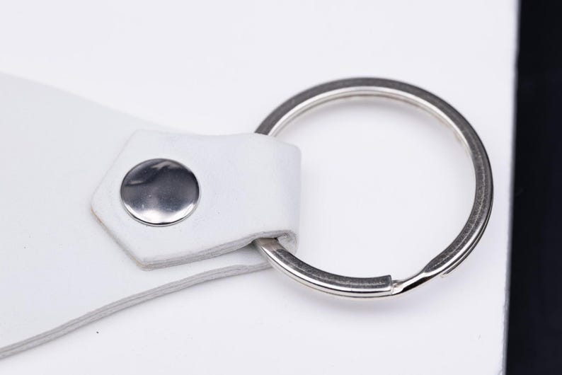 Makroaufnahme des silbernen Schlüsselrings und der feinen Materialstruktur des weißen veganen Kunstleders. Die präzise Verarbeitung zeigt die solide Verbindung zwischen Metall und Kunstleder. Das nachhaltige, vegane Material ist weich, robust und alltagstauglich. Ideal für Schlüssel, Auto oder Tasche – ein personalisierbarer Schlüsselanhänger mit Stil und Bedeutung.