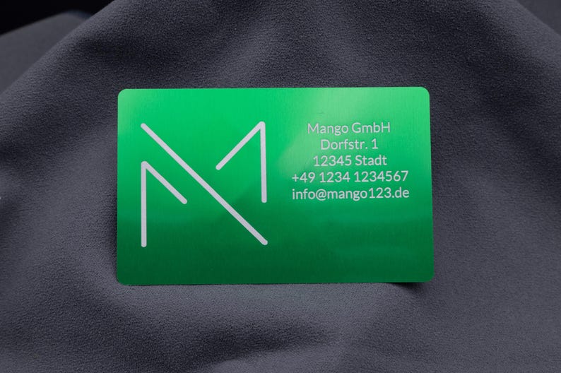 Grüne Visitenkarte aus Metall mit Firmenlogo, Anschrift, Telefonnummer und E-Mail. Das klare, weiße Schriftbild hebt sich gut von der glänzenden Aluminiumoberfläche ab. Die robuste Karte eignet sich hervorragend für den geschäftlichen Einsatz und vermittelt Professionalität, Exklusivität und Beständigkeit, perfekt für Unternehmer, die mit individuellen Visitenkarten auffallen möchten.