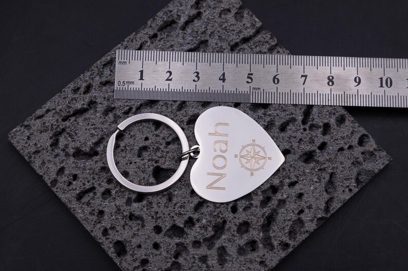 Herz-Schlüsselanhänger aus Edelstahl mit Gravur „Noah“ und Maßband zur Größenangabe. Die Gravur zeigt ein Kompasssymbol und den Namen, während das Maßband die Dimensionen von ca. 4 cm anzeigt. Hochwertige Verarbeitung, glänzende Oberfläche und klare Gravur machen den Anhänger zu einem beliebten personalisierten Geschenk.