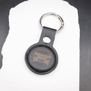 Schwarzer AirTag Schlüsselanhänger aus PU Leder mit graviertem Auto Symbol auf der Vorderseite. Ideal zur Kennzeichnung von Autoschlüsseln. Der Schlüsselanhänger verfügt über einen stabilen Edelstahl Schlüsselring und Druckknopf. Zeitloses Design und präzise Lasergravur machen ihn zu einem praktischen und persönlichen AirTag Zubehör.