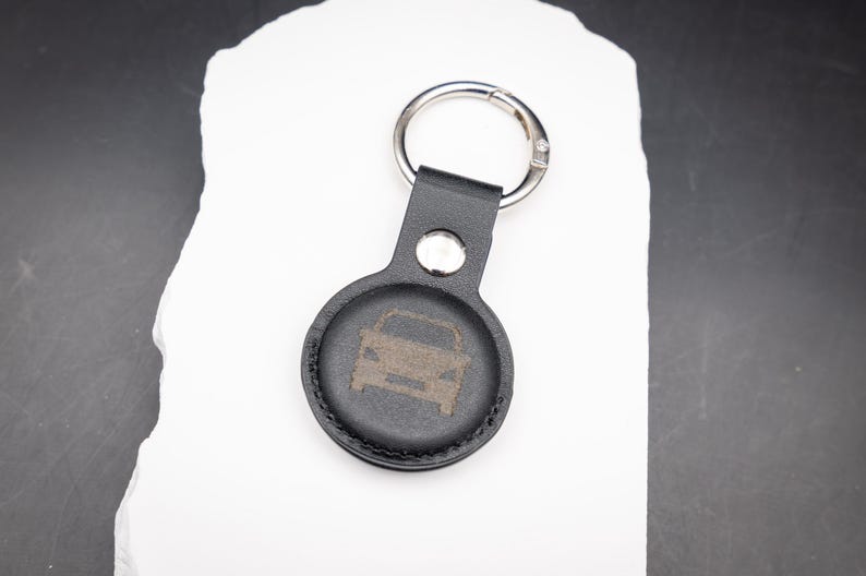 Schwarzer AirTag Schlüsselanhänger aus PU Leder mit graviertem Auto Symbol auf der Vorderseite. Ideal zur Kennzeichnung von Autoschlüsseln. Der Schlüsselanhänger verfügt über einen stabilen Edelstahl Schlüsselring und Druckknopf. Zeitloses Design und präzise Lasergravur machen ihn zu einem praktischen und persönlichen AirTag Zubehör.