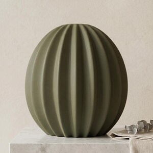 May include: An olive green, spherical vase with vertical ribbed detailing. The vase has a rounded shape and a matte finish. This decorative vase is a home decor item, suitable for display on a table or shelf.