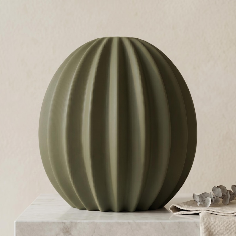 May include: An olive green, spherical vase with vertical ribbed detailing. The vase has a rounded shape and a matte finish. This decorative vase is a home decor item, suitable for display on a table or shelf.