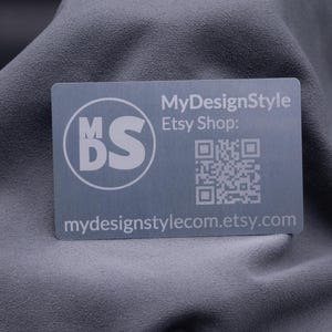 Visitenkarte aus Aluminium in Silber mit matter Oberfläche und Gravur des Logos „MDS“, dem Hinweis auf den Etsy-Shop sowie einem QR-Code. Die edle Metallkarte kombiniert modernes Design mit Funktionalität und ist perfekt geeignet für Unternehmen, Designer und Kreative. Eine langlebige und stilvolle Alternative zur klassischen Papierkarte, ideal für Branding, Networking und Marketingaktionen.