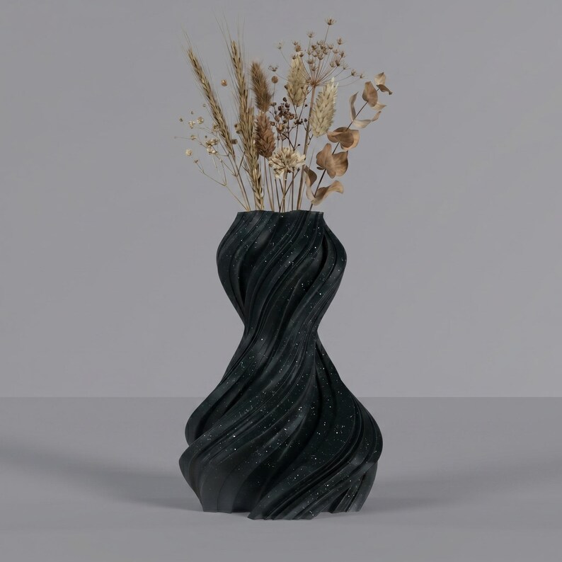 K&ouml;nnte beinhalten: Eine schwarze, strukturierte Vase mit einem Wirbeldesign, &uuml;bers&auml;t mit wei&szlig;en Flecken. Die Vase enth&auml;lt getrockneten Weizen, Gr&auml;ser und Eukalyptuszweige. Die Vase hat eine einzigartige, k&uuml;nstlerische Form und ist ein dekoratives Wohnaccessoire.