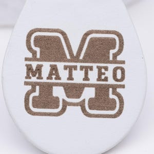 Detailaufnahme des Namens „Matteo“, kunstvoll graviert in goldbrauner Farbe auf weißem veganem Kunstleder. Das Monogramm-Design sorgt für einen eleganten und modernen Look, während die Lasergravur durch Präzision und Klarheit besticht. Der Schlüsselanhänger ist langlebig, angenehm in der Hand und ein ideales personalisiertes Geschenk für Geburtstage, Valentinstag oder als stilvolles Accessoire im Alltag.