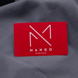 Businesskarte aus rotem Aluminium mit Mango-Digitals-Logo. Die gravierte Metallkarte überzeugt durch ihre matte Oberfläche, edle Optik und langlebige Qualität. Ideal für Start-ups, Designer und Unternehmen, die ihre Marke auf moderne, kreative Weise präsentieren möchten.