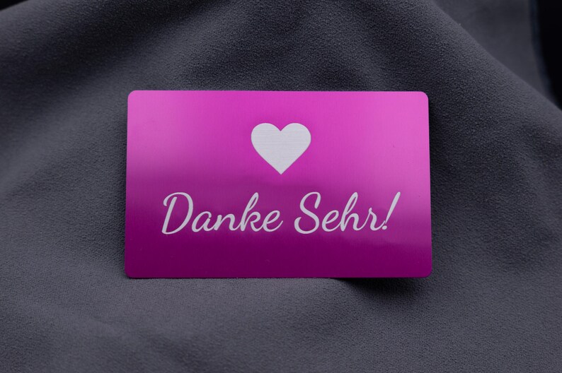 Stilvolle Visitenkarte aus Aluminium in kräftigem Lila mit lasergraviertem Herzsymbol und der Aufschrift „Danke Sehr!“. Die metallische Oberfläche glänzt edel und sorgt für einen besonderen Eindruck. Diese Karte eignet sich hervorragend als Beileger in Bestellungen, als Dankeschön an Kunden oder als besondere Geste im geschäftlichen und privaten Bereich. Robustes Aluminium macht sie langlebig und wiederverwendbar.