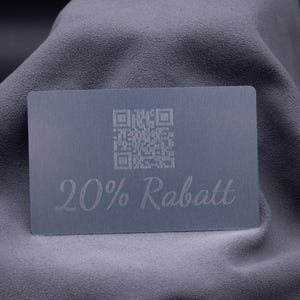 Metallische Rabattkarte aus Aluminium in Silber mit Gravur „20% Rabatt“ sowie QR-Code, auf grauem Stoff präsentiert. Die Karte kombiniert modernes Design mit praktischer Funktionalität, wirkt edel und ist robust im Einsatz. Ideal als exklusive Werbekarte, Gutscheinkarte oder Marketinginstrument für Unternehmen, die ihre Kunden mit einem eleganten und langlebigen Medium begeistern möchten.