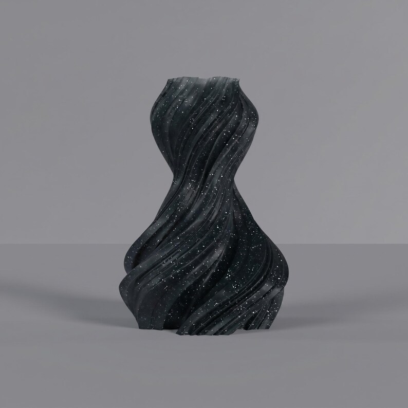K&ouml;nnte beinhalten: Eine schwarze dekorative Vase mit einem wirbelnden, strukturierten Design. Die Vase hat ein gesprenkeltes Muster aus wei&szlig;en Punkten. Die Vase hat eine einzigartige, organische Form. Geeignet f&uuml;r die Inneneinrichtung.