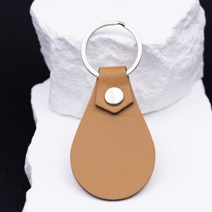 Rückseite eines Schlüsselanhängers aus hellbraunem veganem Kunstleder, schlicht und elegant ohne Gravur. Der silberne Schlüsselring aus Edelstahl und die stabile Niete betonen die hochwertige Verarbeitung. Minimalistisches Design mit langlebigem Material – perfekt für den täglichen Gebrauch an Schlüsselbund, Auto oder Tasche.
