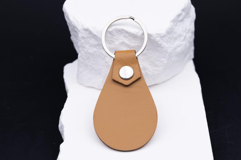Rückseite eines Schlüsselanhängers aus hellbraunem veganem Kunstleder, schlicht und elegant ohne Gravur. Der silberne Schlüsselring aus Edelstahl und die stabile Niete betonen die hochwertige Verarbeitung. Minimalistisches Design mit langlebigem Material – perfekt für den täglichen Gebrauch an Schlüsselbund, Auto oder Tasche.