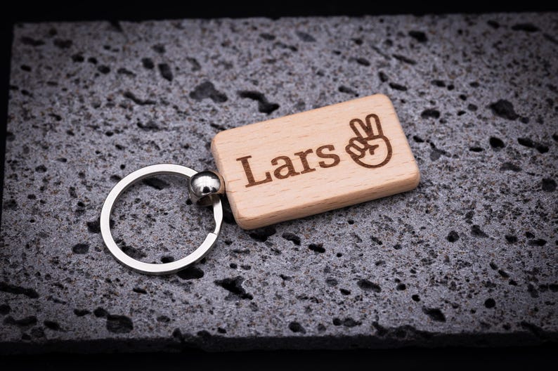 Rechteckiger Schlüsselanhänger aus naturbelassenem Buchenholz, ca. 5 cm lang, personalisiert mit dem Namen Lars und einem Peace-Symbol. Mit präziser Lasergravur gefertigt, stabil verarbeitet und mit abgerundeten Kanten für angenehme Haptik. Der hochwertige Schlüsselring aus Metall sorgt für sicheren Halt. Ein originelles Geschenk für Familie, Freunde oder als individuelles Accessoire für Schlüsselbund, Rucksack oder Handtasche.